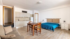 Une pièce comprenant un lit, une table à manger avec des chaises, un canapé, une petite table de chevet et un coin cuisine à l’arrière-plan.