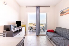 A modern living room with a flat-screen TV, a sofa, a dining table with chairs, and a balcony with a view.