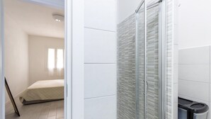 A modern bathroom with a glass shower enclosure, white tiled walls, and a visible trash bin. - Apartment in with swimming pool and sea view (Castelsardo)