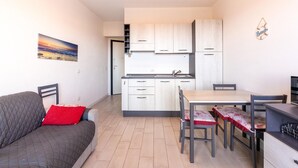 A compact living space with a kitchenette, a dining area, and a sofa with a red pillow. - Apartment in with swimming pool and sea view (Castelsardo)
