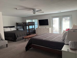A bedroom with a bed, a desk, a chair, a dresser, a television, and a ceiling fan.