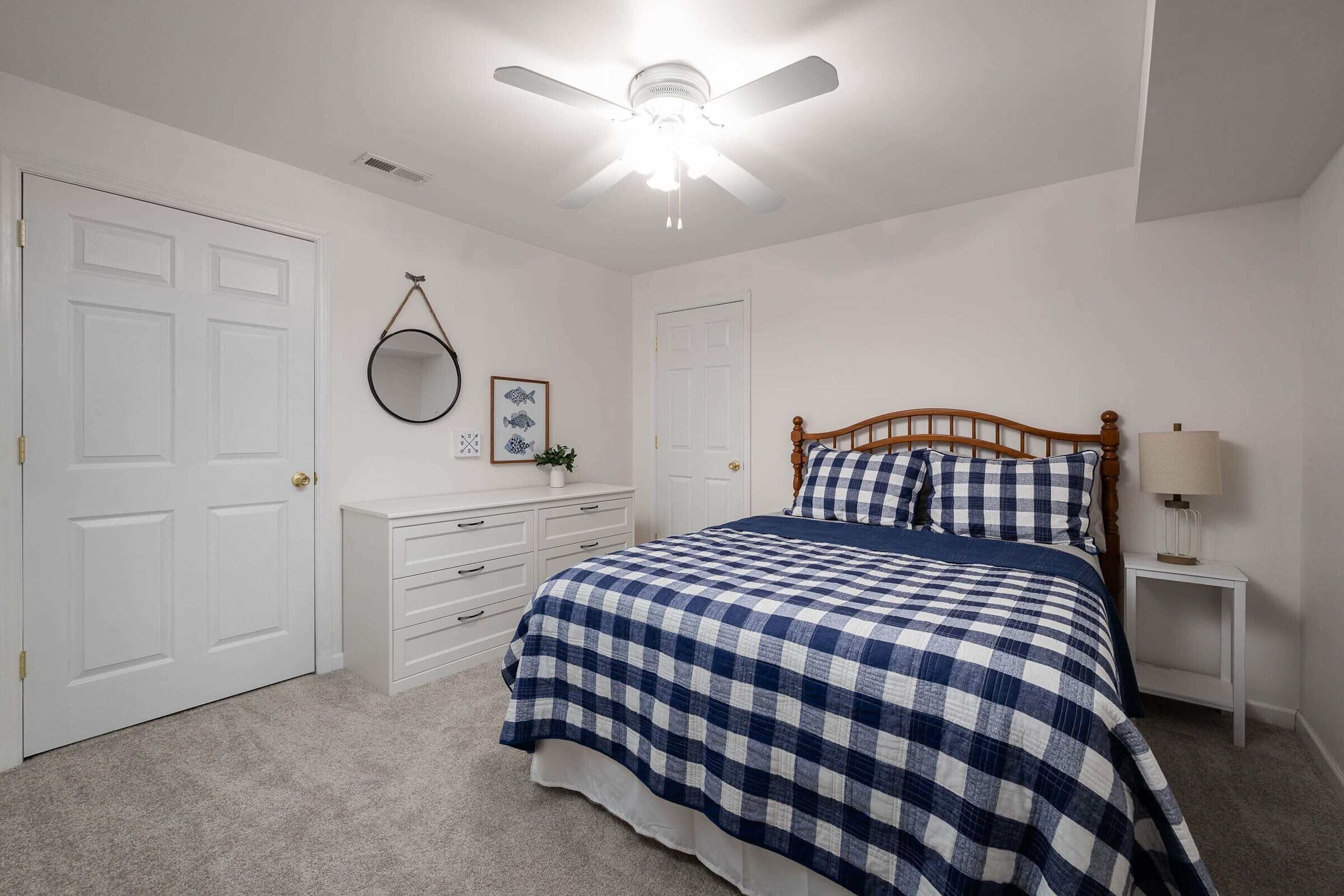 Un dormitorio con cama, cómoda, mesita de noche, ventilador de techo y puerta.