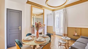 Ein Essbereich mit einem runden Tisch, gedeckt für vier Personen, Stühlen, einer Blumenvase und einem Spiegel über dem Tisch.