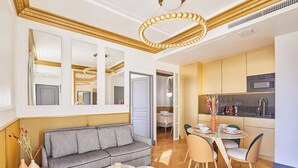 Ein modernes Wohnzimmer mit einer Couch, einem Esstisch mit Stühlen und einer Küchenzeile mit Schränken und Geräten.