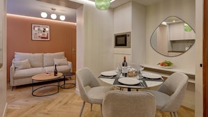 Un salon moderne avec un canapé, une table basse et un coin repas comprenant des chaises et une table dressée pour deux personnes.