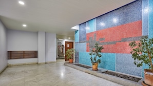 Un hall d’entrée spacieux avec un mur recouvert de carreaux, des plantes en pot et un escalier en arrière-plan.