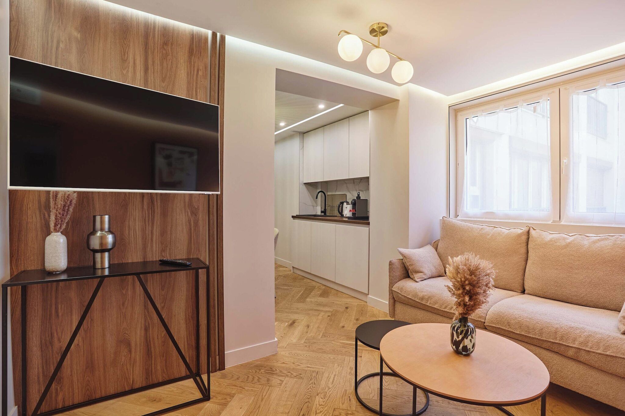 Een moderne woonkamer met een bank, een salontafel en een console met decoratieve objecten. In de achtergrond is een keuken zichtbaar.