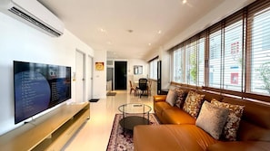 A modern living room with a flat-screen TV, a leather sofa, and a dining area with a table and chairs. - Luxurious 80 sqm Apartment Near Karon Beach with Infinity Pool (Tambon Karon)