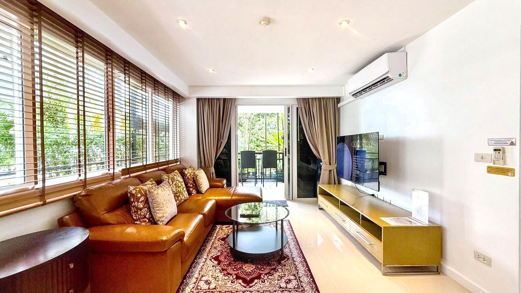 A modern living room with a leather sofa, a glass coffee table, a flat-screen TV, and a sliding glass door leading to an outdoor area.