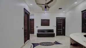 A hallway with a ceiling fan, a dark leather sofa, and a patterned rug. - Hotel Greysky Residency New Delhi (New Delhi)