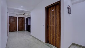 A hallway with two wooden doors, a ceiling fan, and a light fixture on the wall. - Hotel Greysky Residency New Delhi (New Delhi)