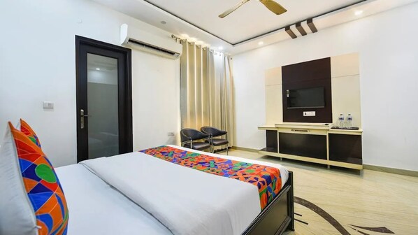 Une chambre d’hôtel avec un lit, un bureau avec une télévision, une chaise et une fenêtre avec des rideaux.