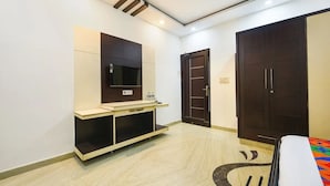 A bedroom with a bed, a TV mounted on the wall, a wardrobe, and a desk with a chair. - Hotel Greysky Residency New Delhi (New Delhi)