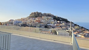 Un pueblo costero con una fortaleza destacada en una colina, edificios residenciales y cielo despejado.