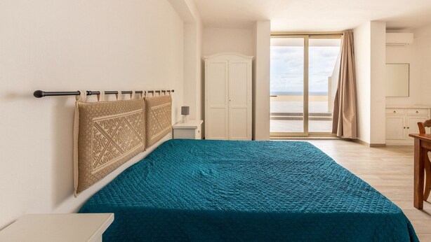 Un dormitorio con cama, armario, escritorio y vistas al exterior.