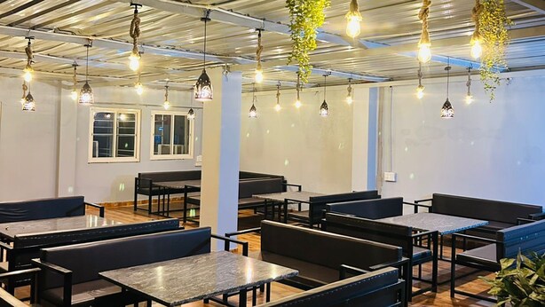Un espace de restauration moderne avec des tables et des bancs en bois, des plantes suspendues et des poutres apparentes au plafond.