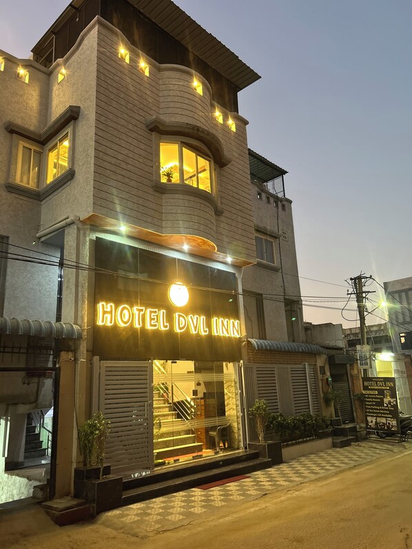 A hotel with a prominent illuminated sign, a staircase leading to the entrance, and a checkered pavement in front. - Hotel DVL INN- Near Jalmahal Jaipur (Jaipur)