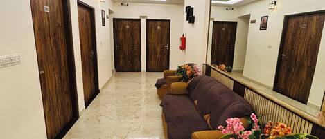 A hotel lobby with a marble floor, wooden doors, a sofa, and a mirror.