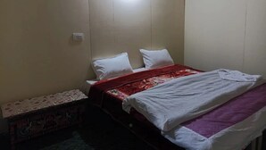 A small, simple bedroom with a single bed, a bedside table, and a wall-mounted light. - Pangong View Point Cottage (Leh)