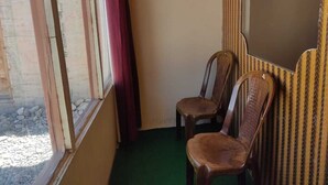 A corner room with two wooden chairs, a window with a red curtain, and a green carpet. - Pangong View Point Cottage (Leh)