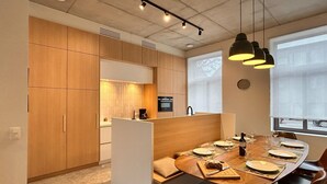 Une cuisine moderne avec des meubles en bois, un coin repas doté d’une table ronde pour quatre personnes et des luminaires suspendus.