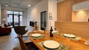 Un espace repas moderne avec une table en bois dressée pour quatre personnes, un canapé et un téléviseur en arrière-plan.