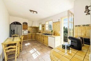 A kitchen with a dining table, chairs, a refrigerator, a sink, and a window. - A/C House 4BR/10P with Pool – 40 min from Cannes (Le Tignet)