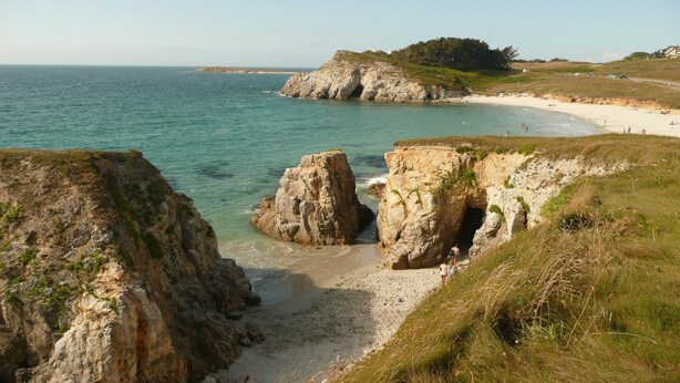Un paysage côtier caractérisé par des formations rocheuses, une plage de sable et une vue dégagée sur la mer.