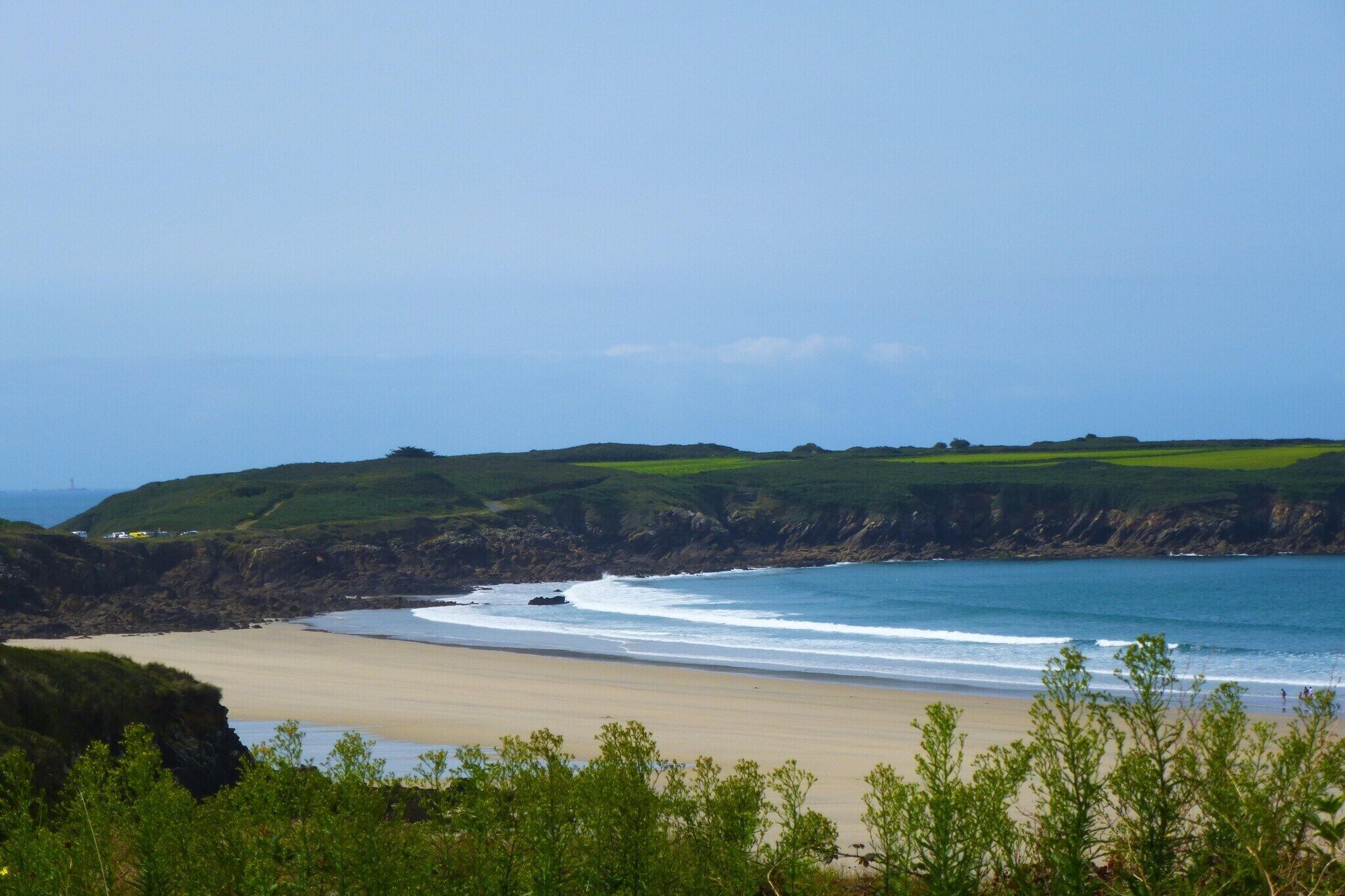 Un paysage côtier avec une plage de sable, des collines verdoyantes et un ciel dégagé.