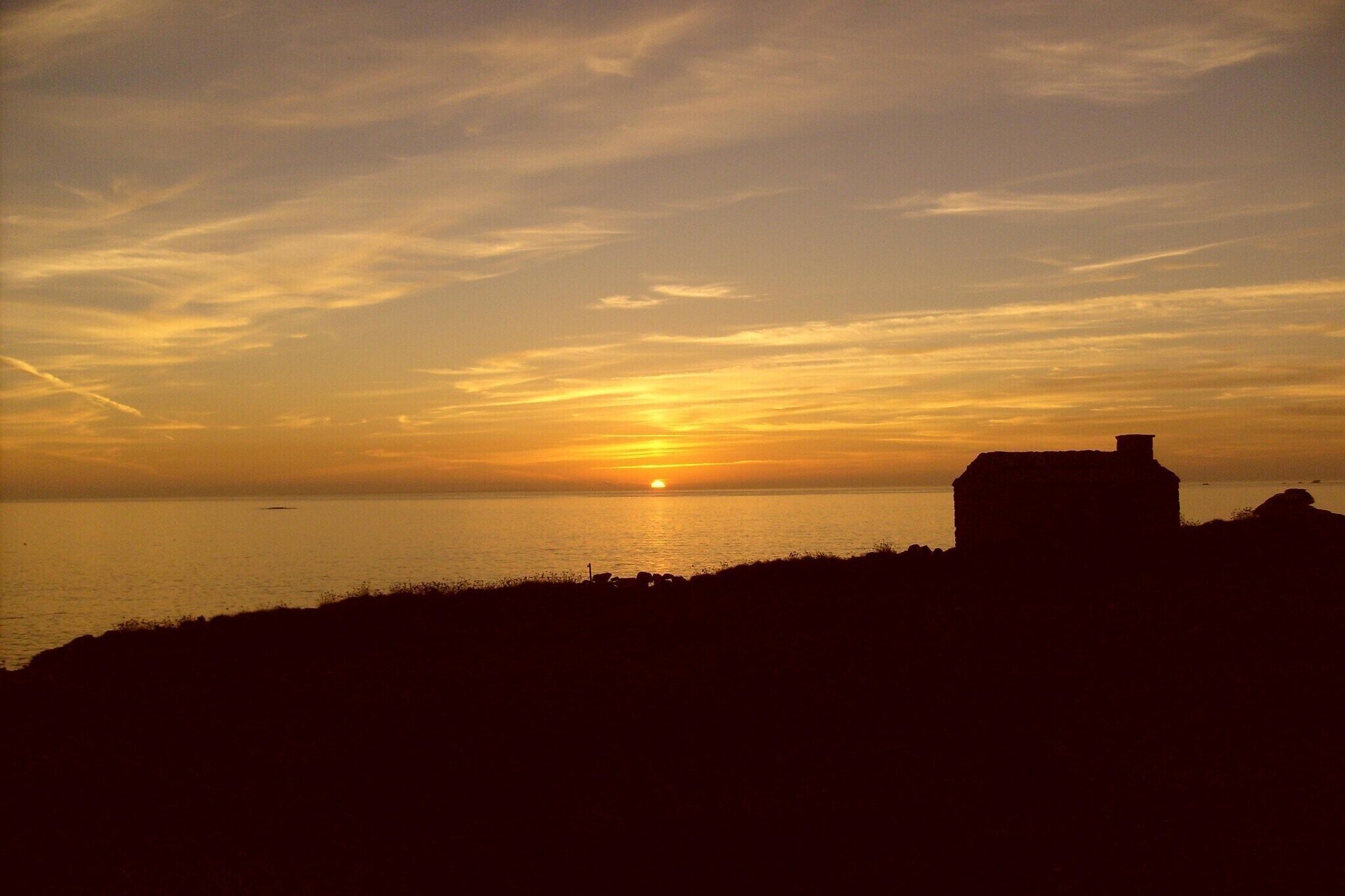 Een zonsondergang boven het water, met een gebouw in silhouette aan de rechterkant.
