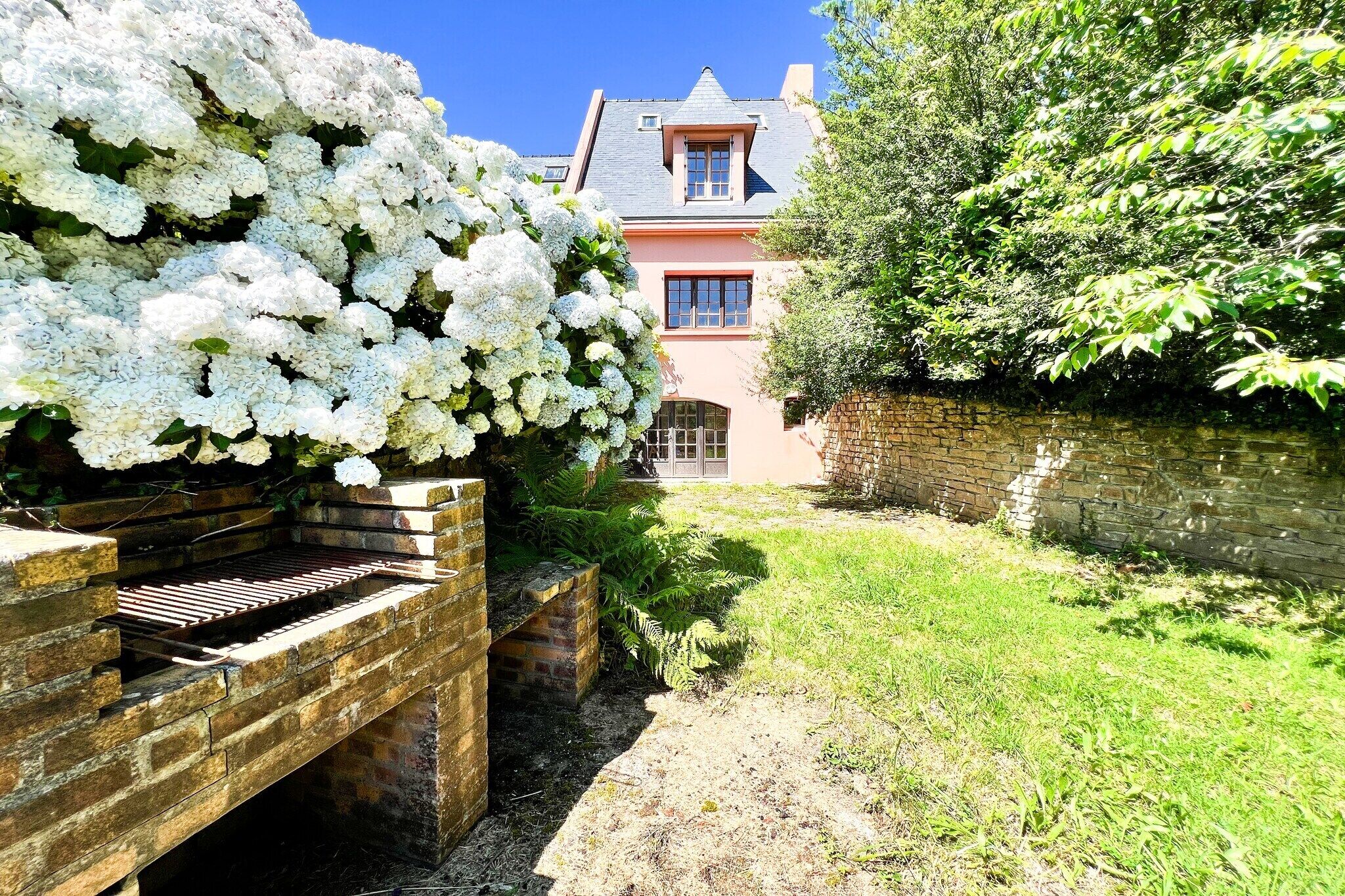 Un barbecue en briques, un mur en briques et une maison à la façade rose et au toit gris.