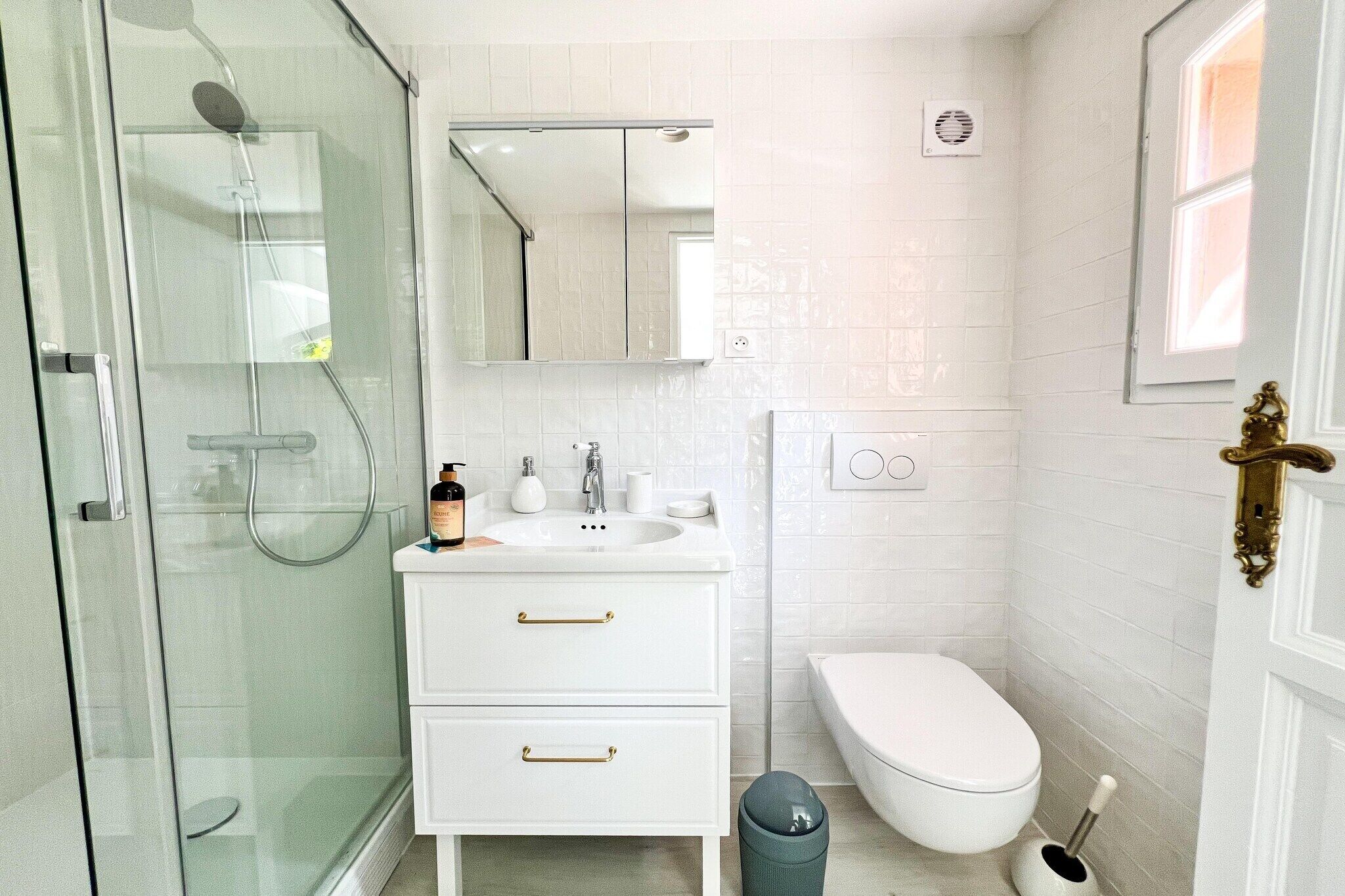 Un baño moderno con ducha envuelta en vidrio, un lavabo blanco con detalles dorados y un inodoro.