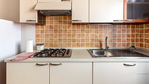 A kitchen with a gas stove, a sink, and a tiled backsplash. - 150 meters from the sea, 2 swimming pools (Valledoria)