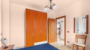 A bedroom with a bed, wooden wardrobe, chair, and a mirror. - 150 meters from the sea, 2 swimming pools (Valledoria)