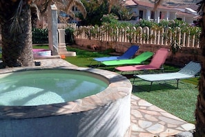 Ein Swimmingpool mit Steingrenze, umgeben von einer Steinterrasse und drei Liegestühlen.