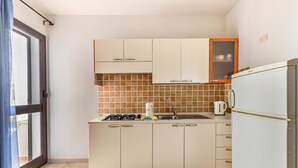 Een compacte keuken met witte kastjes, een betegelde spatwand, een gasfornuis, een spoelbak en een koelkast.