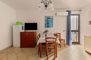 A dining area with a table, chairs, a television, a cabinet, and a poster on the wall. - 150 meters from the sea, 2 swimming pools (Valledoria)