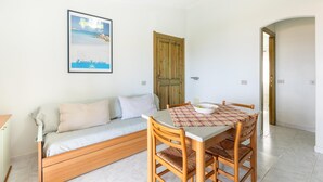A room with a wooden sofa, a dining table with chairs, a framed picture on the wall, and a wooden door. - 150 meters from the sea, 2 swimming pools (Valledoria)