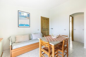 A room with a wooden sofa, a dining table with chairs, a framed picture on the wall, and a wooden door. - 150 meters from the sea, 2 swimming pools (Valledoria)