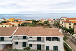 Een woongebied aan de kust met terracotta dakpannen, helder uitzicht op zee en een verzorgde straat.