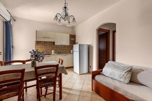 Een eethoek met een tafel, stoelen en een bloevas. Achtergrond is een kitchenette met kastjes en een koelkast.