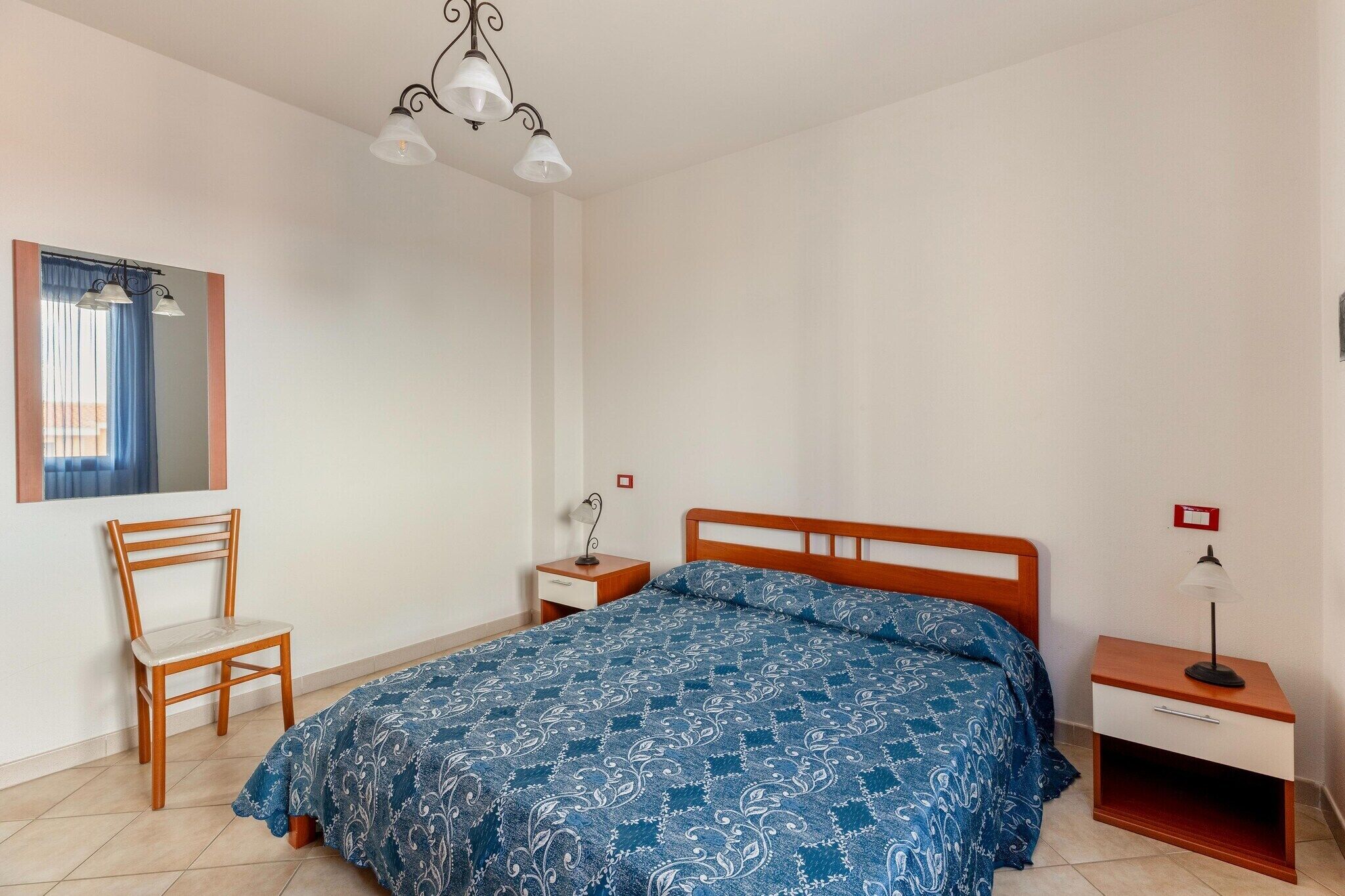 Ein Schlafzimmer mit einem Bett, einem Sessel, einem Nachttisch, einer Lampe und einem Spiegel.