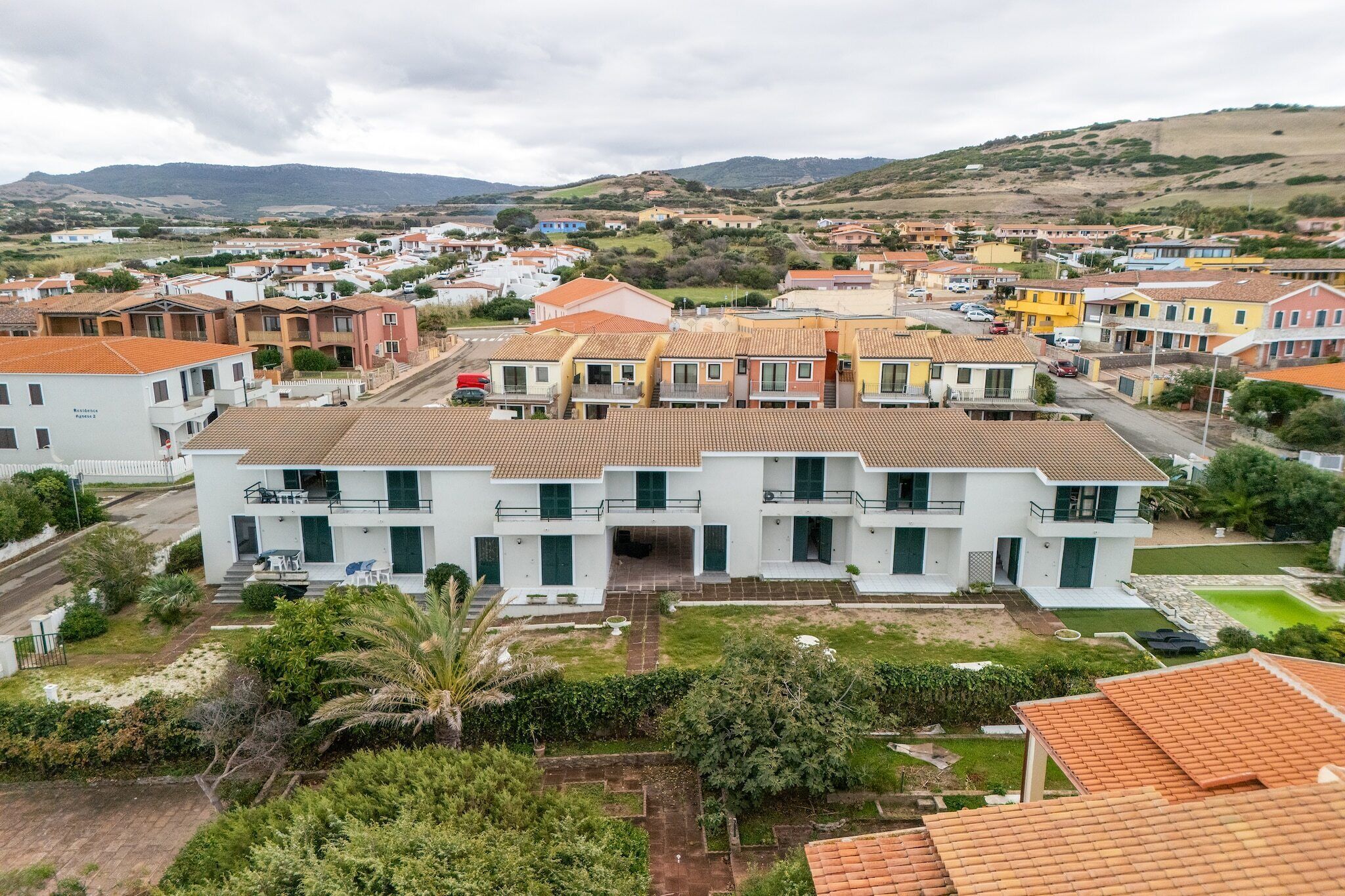 Un quartiere residenziale con diversi edifici a due piani, una strada centrale e vegetazione circostante.