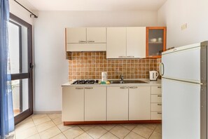 A compact kitchen with white cabinets, a tiled backsplash, a gas stove, a sink, and a refrigerator. - 150 meters from the sea, 2 swimming pools (Valledoria)