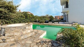 Ein Pool mit Steinstufen, umgeben von Grünflächen und einem weißen Gebäude mit Balkon.