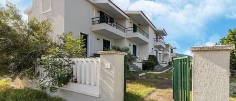 A multi-story residential building with balconies, a gated entrance, and a pathway leading to the entrance.