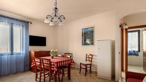 Uma sala de jantar com uma mesa posta para quatro pessoas, um lustre, uma televisão na parede e um cartaz.