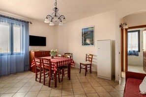 Ein Essbereich mit einem Tisch für vier Personen, einer Chandelüster, einem an der Wand befestigten Fernseher und einem Poster.