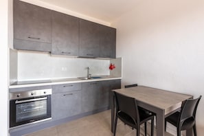 A modern kitchen with grey cabinets, a built-in oven, and a dining area with a table and chairs. - Air-conditioned, in residence, with pool and patio (Castelsardo)