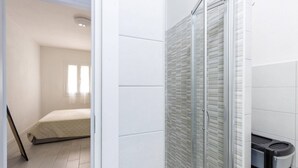 A modern bathroom with a glass shower enclosure, white tiled walls, and a visible trash bin. - Apartment in with swimming pool and sea view (Castelsardo)